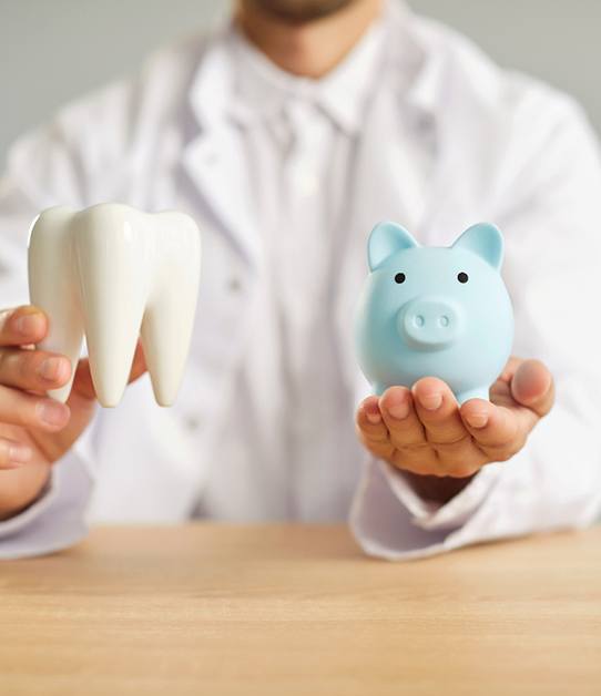 Man in white jacket holding model tooth and piggy bank