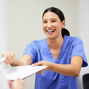Woman handing insurance forms on clipboard to dentist