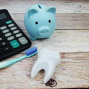 Blue piggy bank, toothbrush, model tooth, and calculator on wooden surface