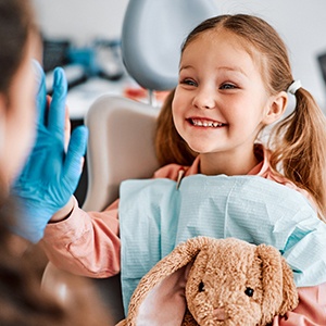 A little girl smiling and holding a stuffed bunny at dentist’s office