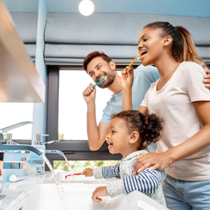 Man, woman, and little girl all brushing teeth together at double bathroom sinks