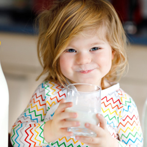Toddler in zig-zag shirt drinking glass of milk next to milk bottles