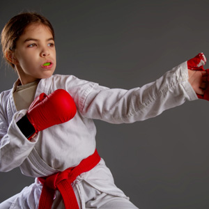 Girl in white uniform with red gloves and belt wearing green mouthguard
